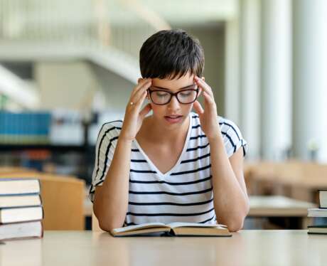 Exhausted young female studying and preparing for exam in college library. Education people concept