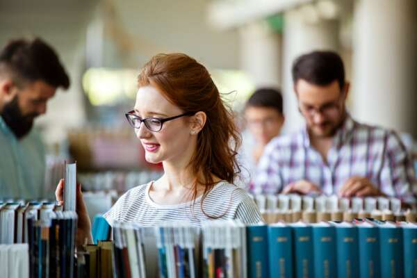 Happy university students studying with books in library. Group of multiracial people in college