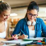 Happy young students studying and preparing for exam in college library. Education people concept