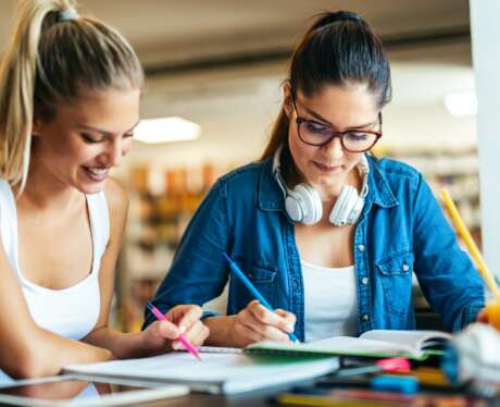 Happy young students studying and preparing for exam in college library. Education people concept