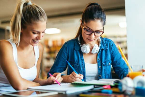 Happy young students studying and preparing for exam in college library. Education people concept